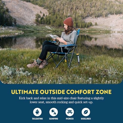 Woman sitting in a chair reading by a lake with mountains in the background.